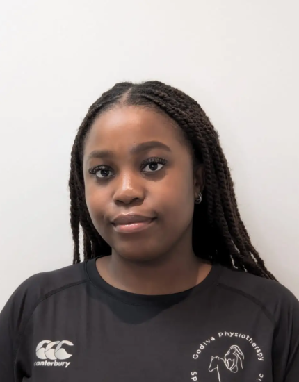 A person with long braids is wearing a black shirt with a logo. They are standing against a plain, light-colored background.